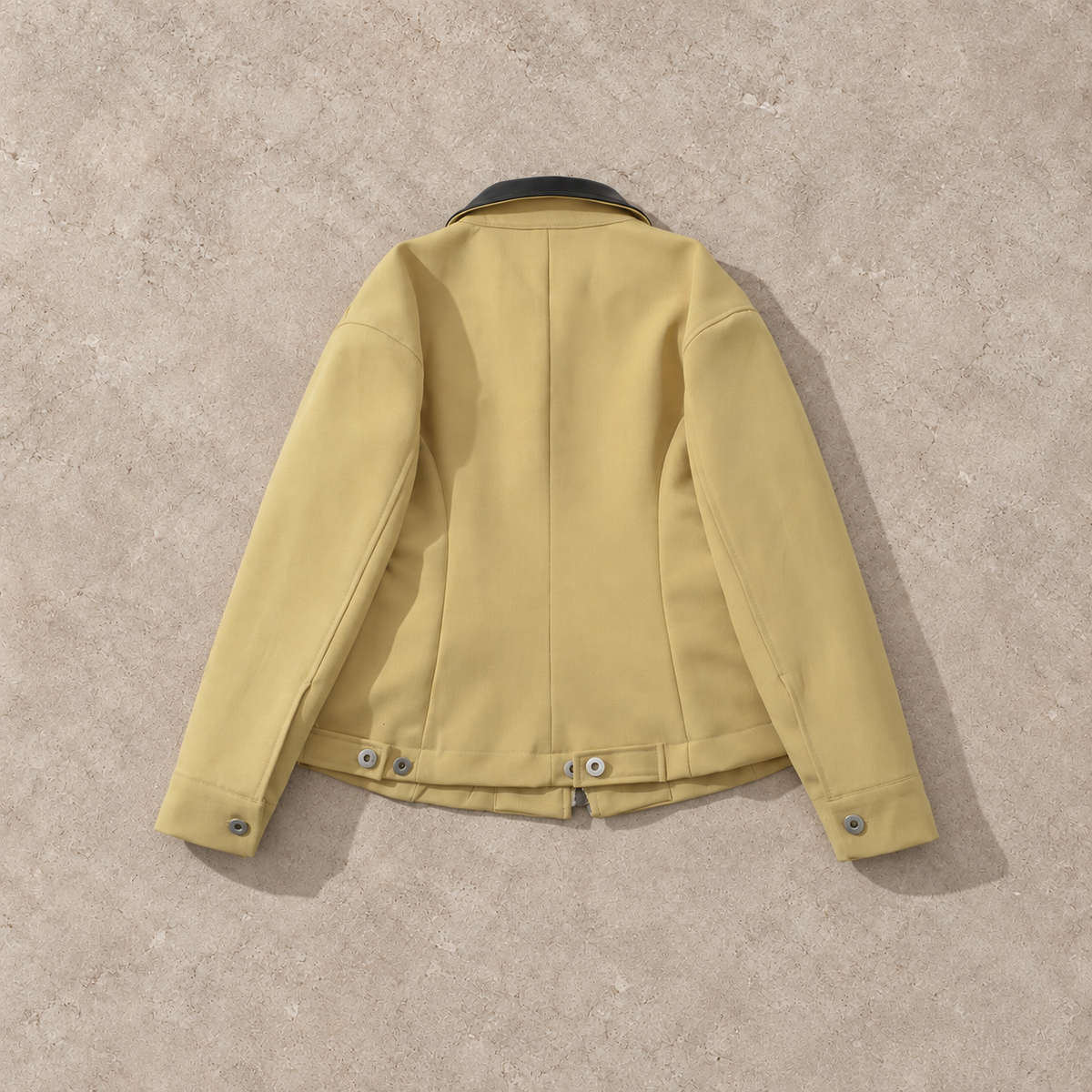 Veste courte jaune à col contrastant, vue de dos sur fond pierre